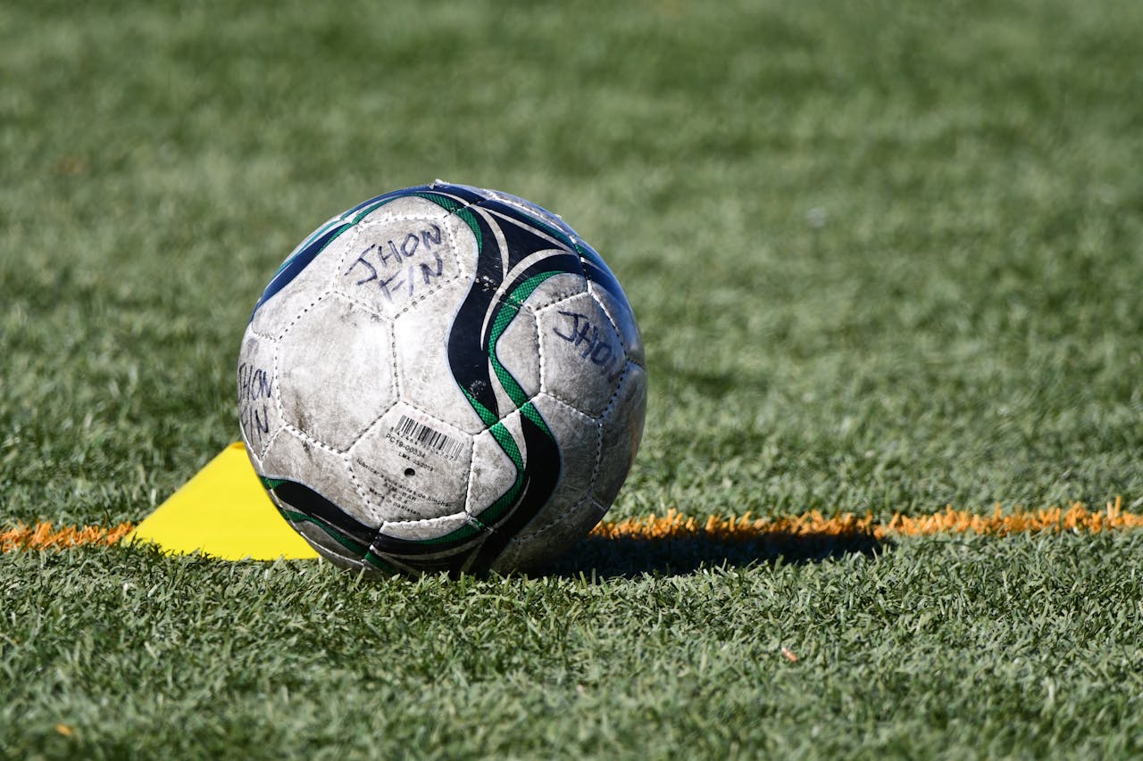 Close-up of a soccer ball resting on a grass field with a yellow marker.